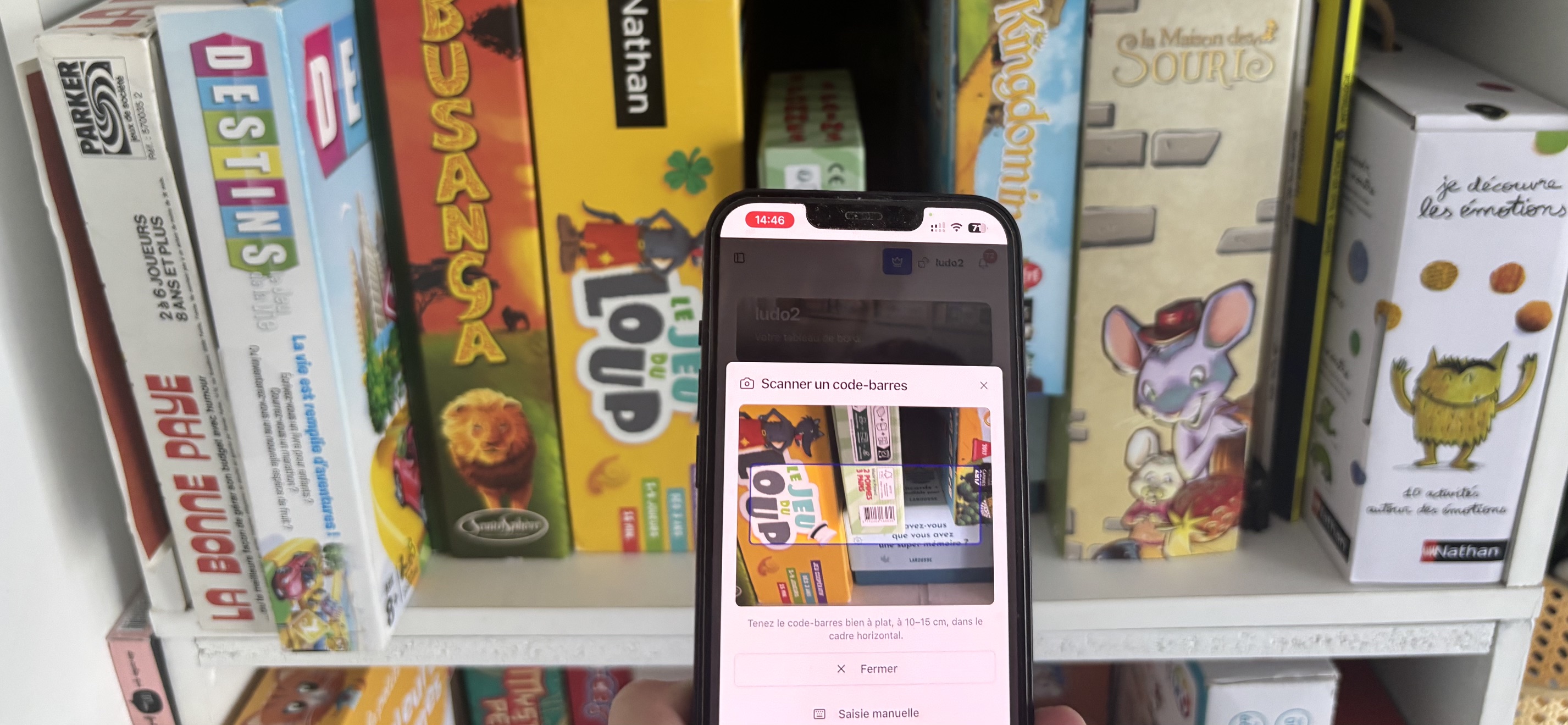 Scanner codes-barres Cubelya sur smartphone devant un rayon de jeux en ludothèque